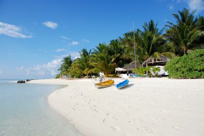 a white sandy beach with two boats and palm trees in the background , under a clear blue sky at Vilamendhoo Island Resort & Spa