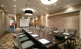 a conference room with a long table and chairs , along with a projector screen on the wall at Kings Hotel