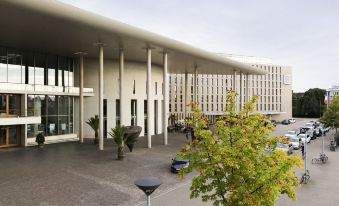 a modern building with a large courtyard in front of it , surrounded by trees and benches at Novotel Freiburg am Konzerthaus