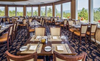 a large dining room with multiple tables and chairs , all set for a meal , surrounded by windows that offer a view of the outdoors at White Mountain Hotel and Resort