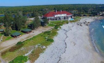 a large white building with a red roof is surrounded by trees and has a beach in front at White Point Beach Resort
