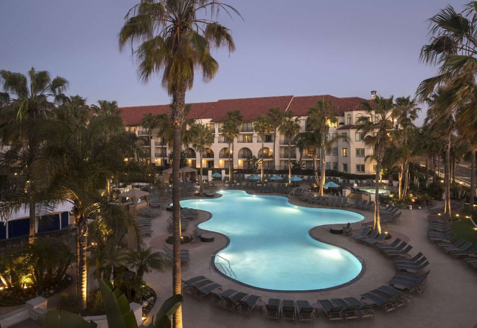 a large hotel with a pool surrounded by palm trees and lounge chairs , lit up at night at Hyatt Regency Huntington Beach Resort and Spa