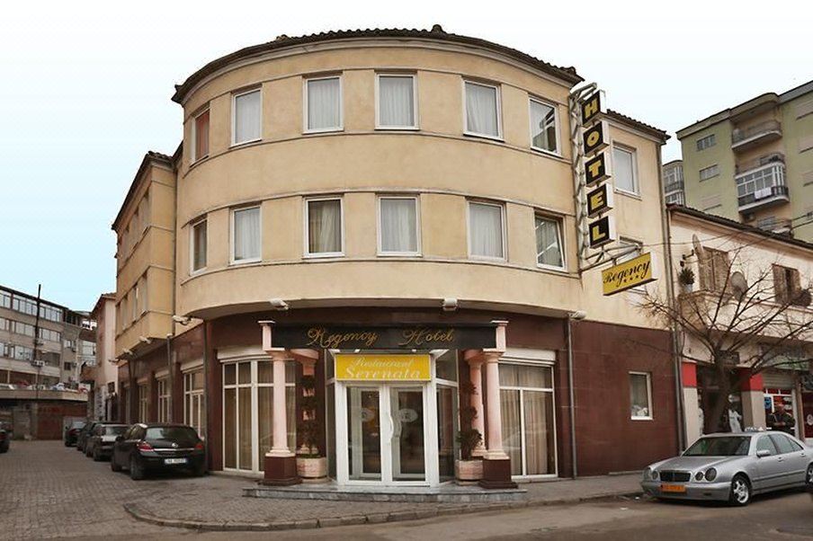 a modern building with a curved facade , large windows , and a yellow sign above the entrance at Hotel Regency
