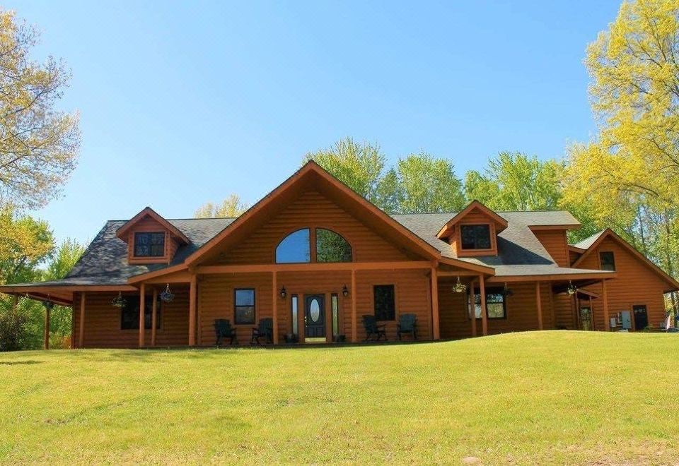 a large wooden house surrounded by green grass and trees , with a grassy field in front of it at Oak Creek Lodge