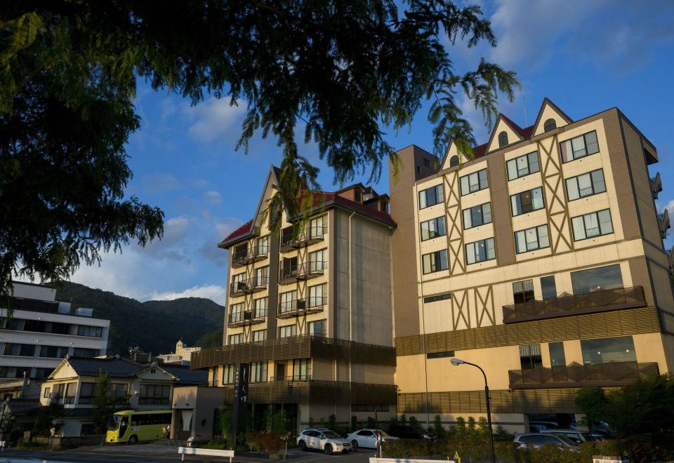 a large building with multiple floors and windows , situated in front of trees and mountains at Kamisuwa Onsen Shinyu