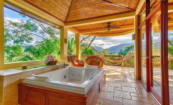 a hot tub is situated on a balcony with a view of the mountains , and two chairs at Sleeping Giant Rainforest Lodge