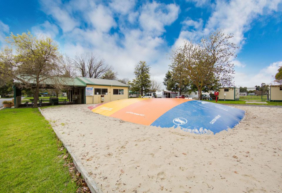 a sandy playground with a slide , swings , and other play equipment , surrounded by grass and trees at Big4 Borderland Wodonga