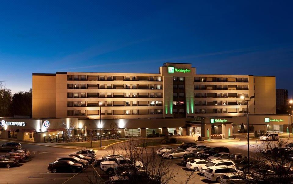 a large hotel with a green roof is illuminated at night , surrounded by parked cars and trees at Holiday Inn Laval - Montreal