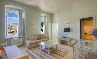 a spacious living room with a large window , a couch , a tv , and a dining table at Hydra Hotel