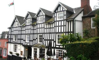 a black and white half - timbered building with a patio area in front , surrounded by greenery at The Dragon Hotel