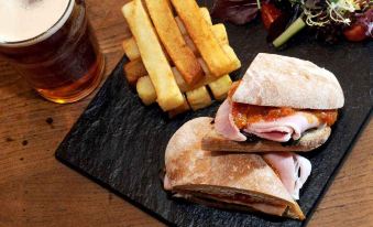 a plate of food consisting of ham , cheese , and fries , accompanied by a glass of beer at The Coachman Inn