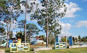 a playground with wooden benches and colorful structures , surrounded by trees and a clear blue sky at Colony