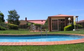 a large swimming pool with a red roof and wooden deck is surrounded by green grass , trees , and a building at Grange Burn Motel