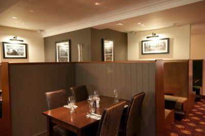 a dining room with a wooden table and chairs , surrounded by framed pictures on the wall at Village Hotel Liverpool