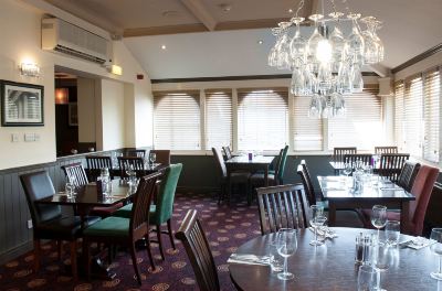 a large dining room with multiple tables and chairs , a chandelier , and windows on the right side at Village Hotel Liverpool