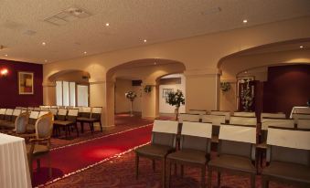 a large , well - lit room with rows of chairs arranged for an event or meeting , surrounded by white columns and a red carpet at The Gibside Hotel