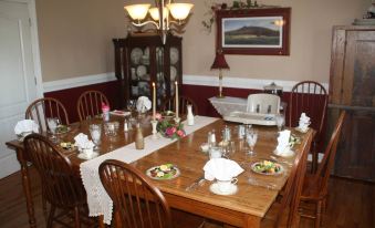 a dining room with a large wooden dining table , surrounded by chairs , set for a meal at A Mighty Oak B&B