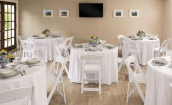 a dining room with white tablecloths and chairs , a tv on the wall , and framed pictures at The Jacqueline House of Wilmington