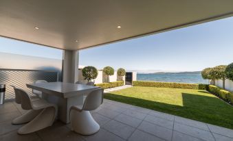 a large outdoor patio with a dining table and chairs , surrounded by a grassy area and a body of water at Sacred Waters Taupo