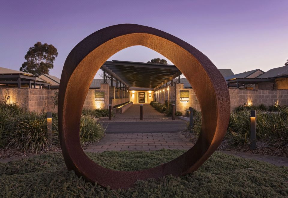 a large circular metal sculpture in front of a building at dusk , surrounded by greenery at The Louise