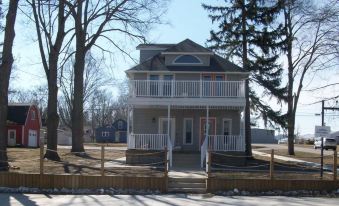 a two - story house with a wrap - around porch and two balconies is surrounded by trees and a wooden fence at Devils Lake Inn