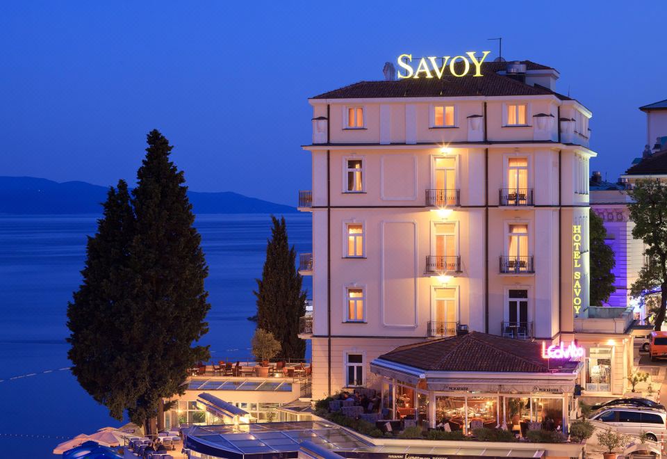 "a large hotel with a hotel sign that says "" savoy "" is surrounded by trees and water at night" at Hotel Savoy