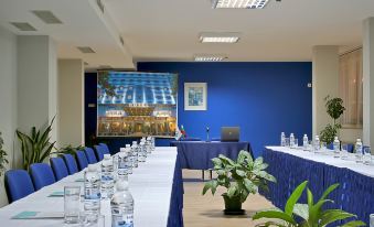 a long table with blue chairs and water bottles in front of a large screen at Aqua Hotel