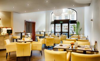 a restaurant with yellow chairs and tables , a large window , and a green plant on the table at Hotel National