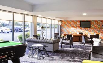 a modern lounge area with a pool table , couches , and chairs , as well as a large window providing natural light at Ibis Styles Barnsley