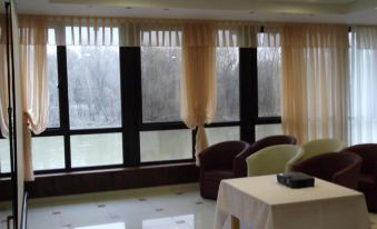 a room with two chairs , a table , and large windows covered by curtains , all set against a white tiled floor at Alfa Hotel