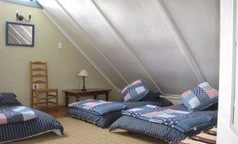 a cozy attic room with two beds , one of which is made up with blue and white striped bedding , and a small wooden table at MRS Simpson
