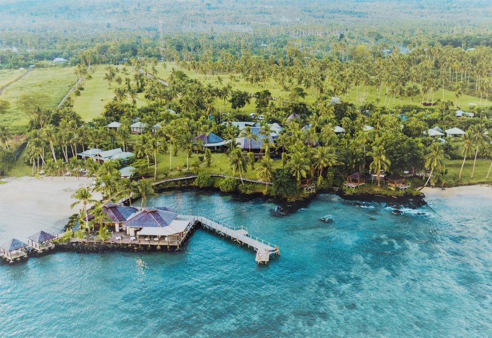 a tropical island with lush greenery and blue water , as well as a wooden pier extending into the ocean at Sinalei Reef Resort & Spa