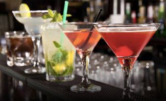 a bar counter with a variety of colorful drinks , including two martini glasses and a cocktail glass at Hotel Alpino