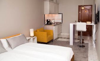 a modern hotel room with white walls , wooden furniture , and a yellow armchair , featuring a bed , desk , and kitchenette at La Palmera Rooms