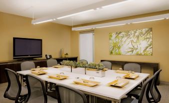 a large white table is set with plates , cups , and napkins in a room with a television at Element Lexington