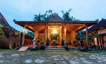 a wooden house with a covered porch , surrounded by palm trees and lit up at night at Astuti Gallery Homestay