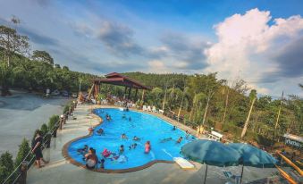 a large outdoor swimming pool surrounded by trees , with several people enjoying their time in the water at Palmsuay Resort