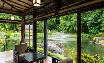 a room with a large window overlooking a pond and trees , featuring two chairs and a table at Ryugon