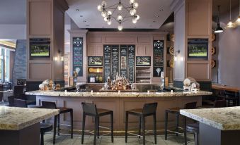 a bar with several stools and chairs , along with a chandelier hanging from the ceiling at Raleigh Marriott City Center