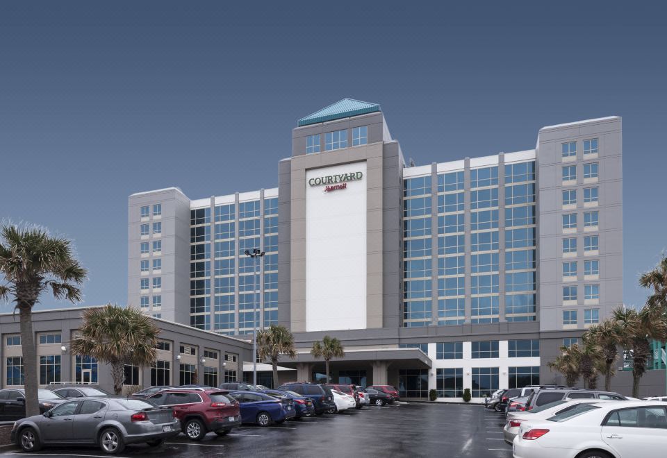 a large hotel building with a parking lot in front of it , surrounded by trees at Courtyard Carolina Beach Oceanfront