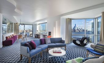a modern living room with a blue couch and chairs , a dining table , and a view of the city at W Hoboken