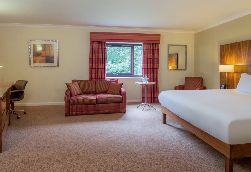 a well - decorated hotel room with a bed , couch , and window , along with some artistic artworks on the walls at Delta Hotels Milton Keynes