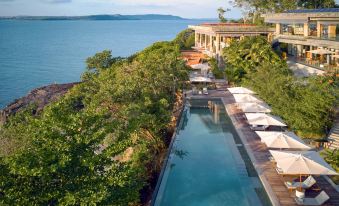 a long pool is surrounded by lounge chairs and umbrellas , with a building in the background at Six Senses Krabey Island