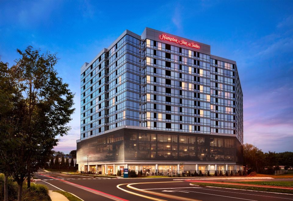 a large hotel with a red sign on top , surrounded by trees and lit up at night at Hampton Inn & Suites Teaneck Glenpointe