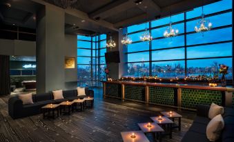 a modern lounge area with large windows , couches , and tables , as well as a bar with wine glasses and candles at W Hoboken
