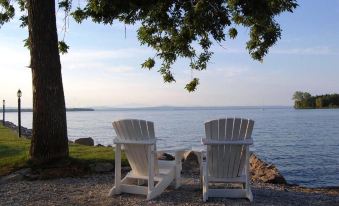 two white adirondack chairs are facing each other on a beach , with the ocean in the background at The North Hero House Inn & Restaurant