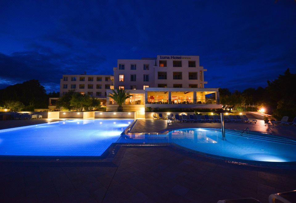 a large swimming pool with blue water is in front of a hotel at night at La Luna Hotel - All Inclusive