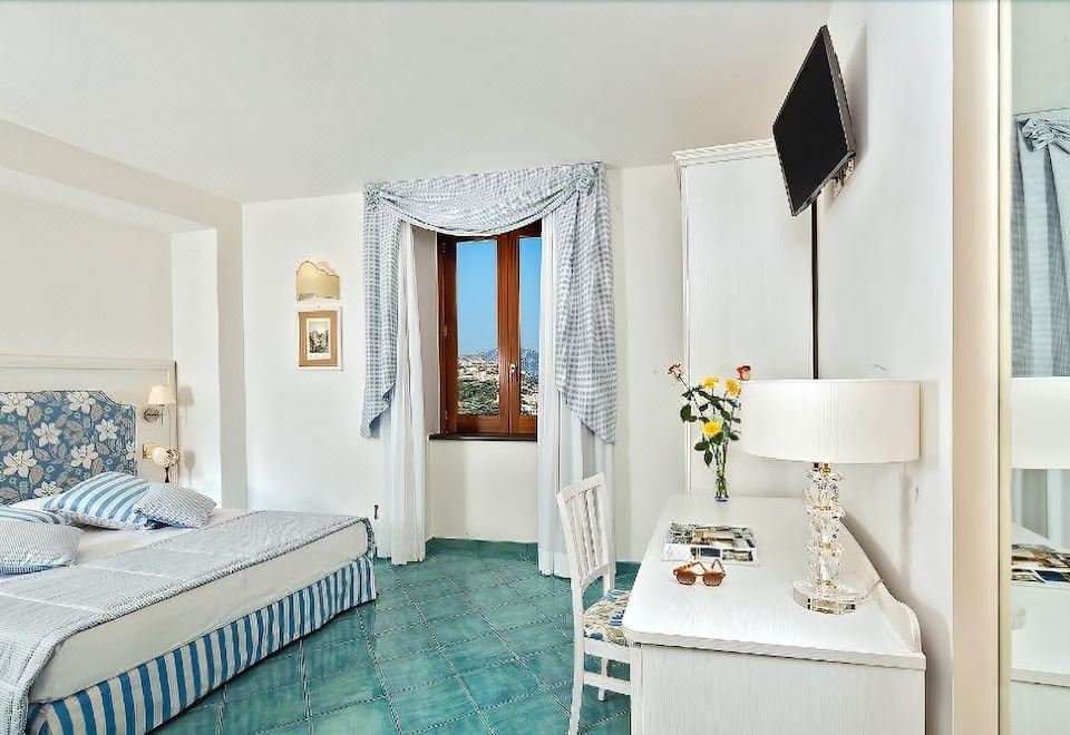 a hotel room with a large window , white walls , and blue flooring , featuring a bed , desk , tv , and other amenities at Villa Maria