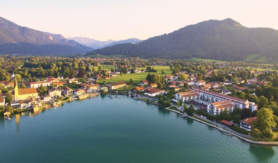 a bird 's eye view of a village nestled by the water with mountains in the background at Althoff Seehotel Überfahrt