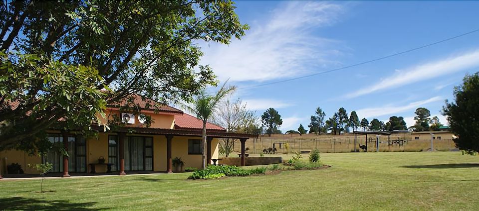 a house with a red roof is surrounded by green grass and trees , while a fence is visible in the background at Mountain View Guest House